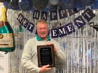 Man holding a plaque in front of a banner that says Happy Retirement