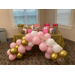 a table with a gold table cloth, a pink, gold and white balloon arch and presents in pink, gold and white gift bags