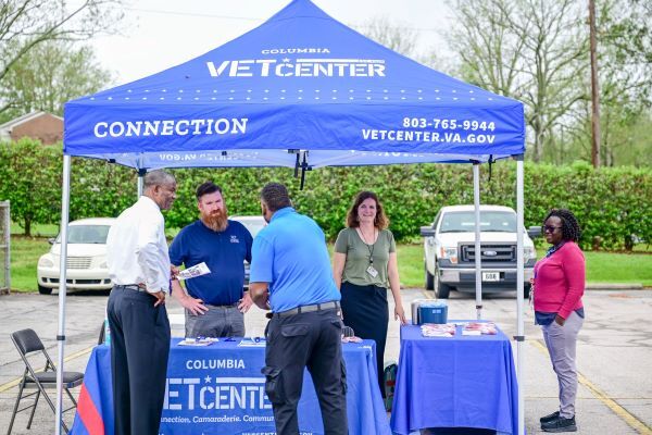 Vet Center Tent with tables and a group of people standing around them talking. 