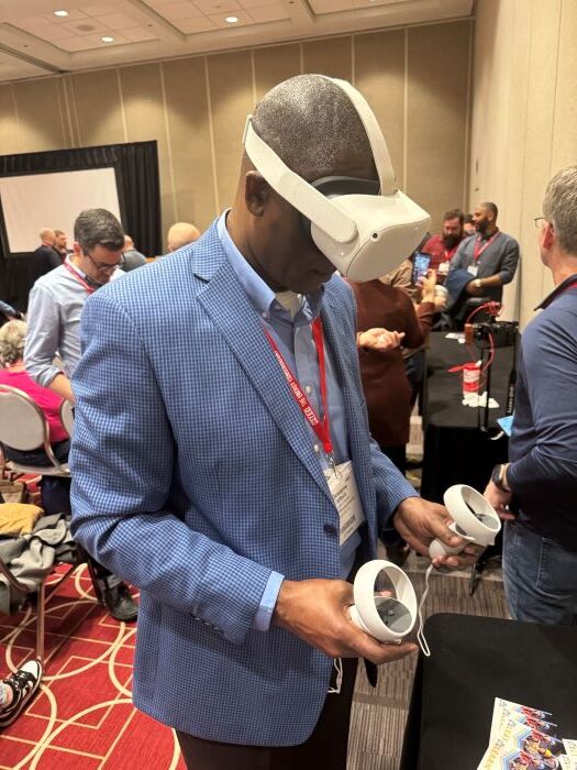 Mr. Dewayne Alford is looking down towards the floor and wearing a virtual reality headset and using hand controllers. 