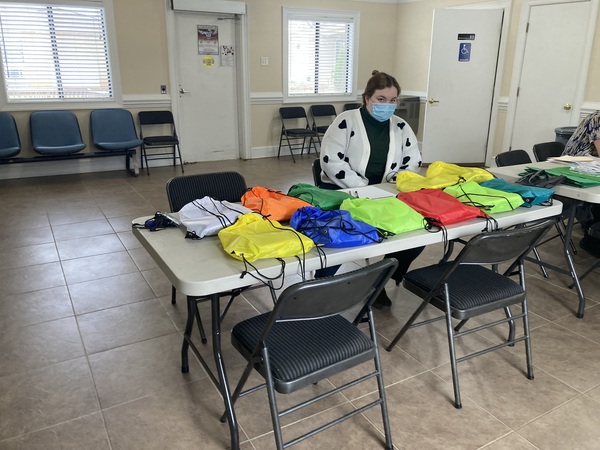 Woman sitting at a table full of backpacks.