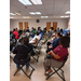 Many people in folding chairs, listening to someone speak.