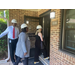 Men and women walk through the door of an apartment from the outside, each with a hardhat on. 