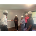 A man talks with the group while in a room of an apartment. Each are wearing a hardhat.