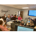 A group of people talking in a conference room with a large monitor on the wall and a graphic on the wall with the word Teamwork. 